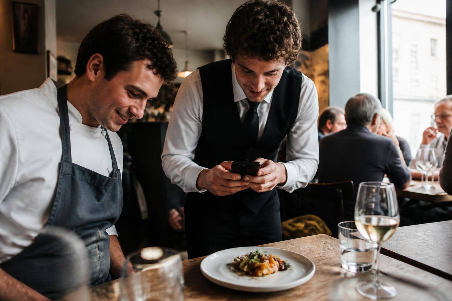 Chef and waiter taking photos of food in a small bistro